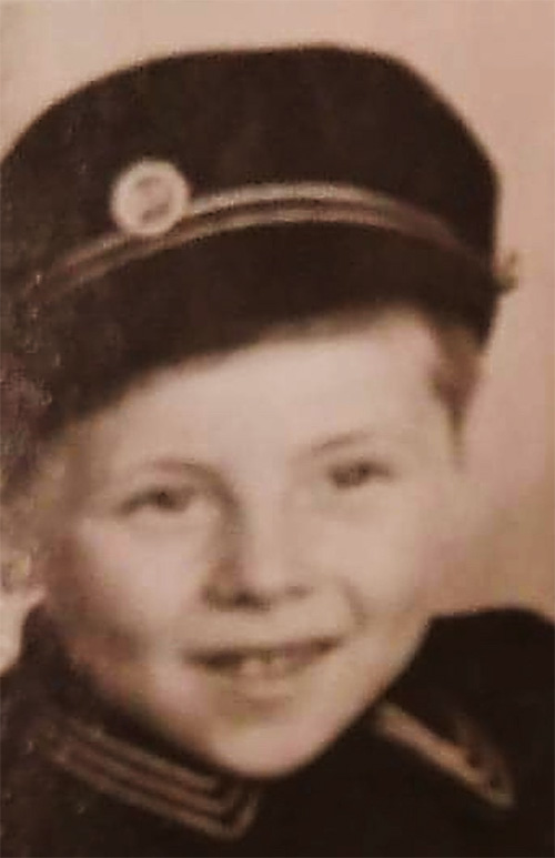 Un petit garçon portant une jolie casquette et un uniforme sourit à la caméra.