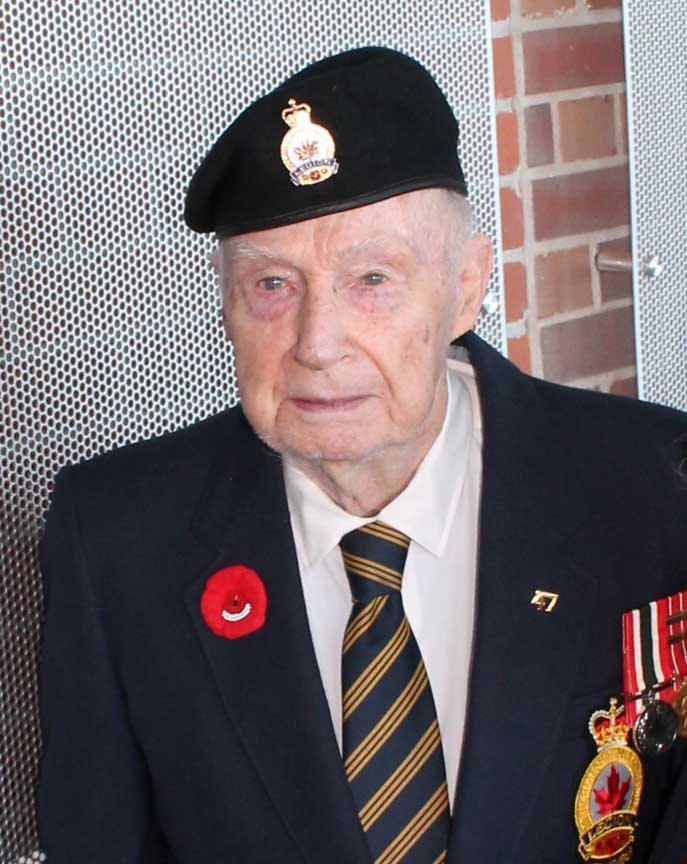 Un ancien combattant portant un béret et des médailles devant le Mur du service.