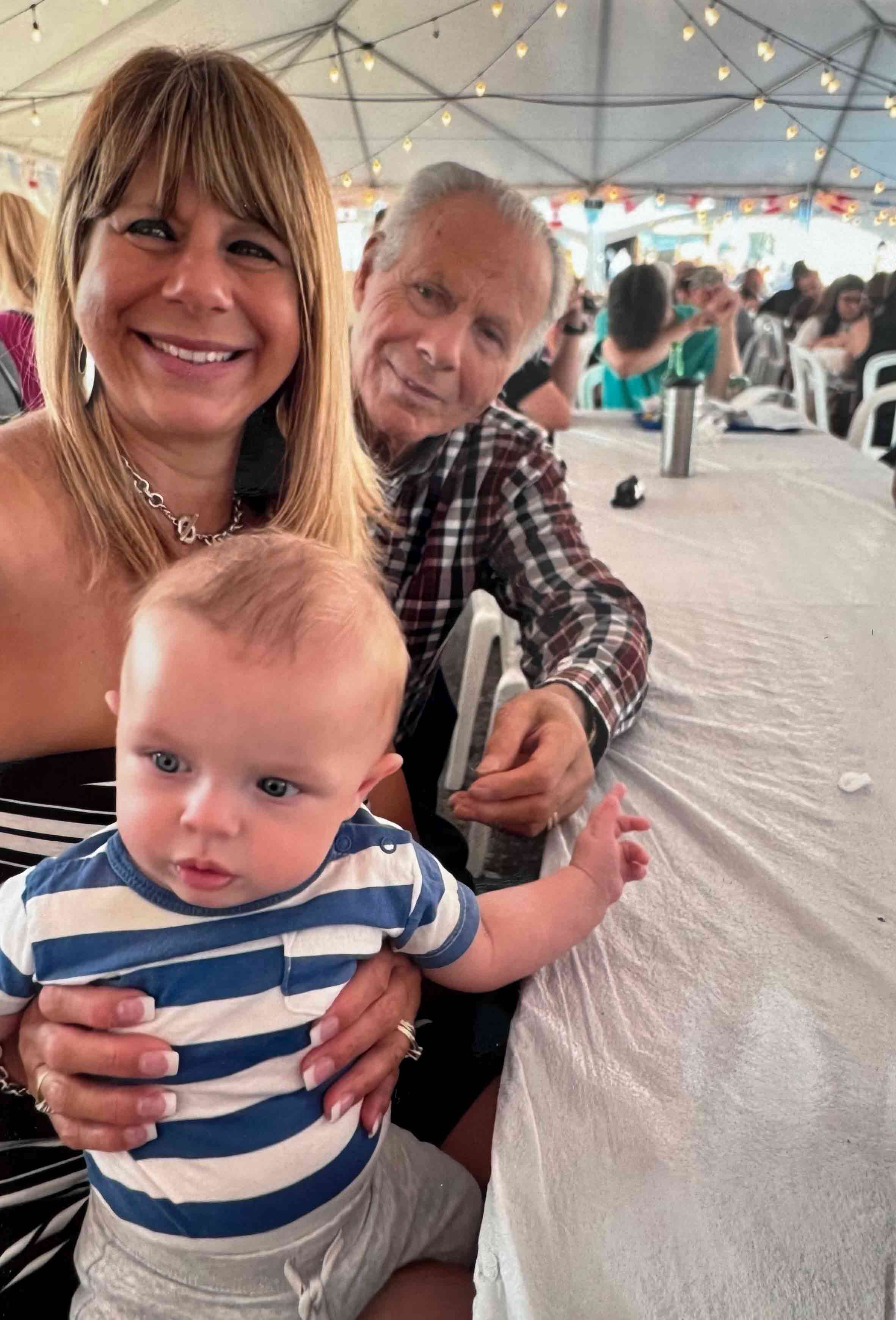 Un homme grec souriant, une femme et un bébé assis à une longue table.