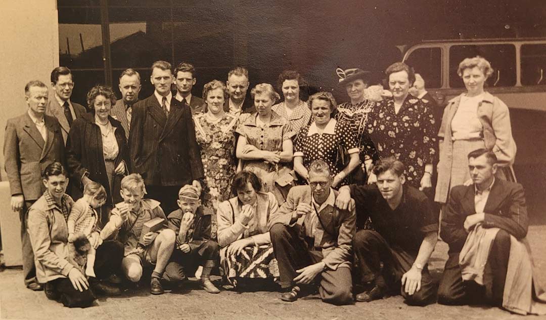 Photo en tons sépia d’un grand groupe de Néerlandais sur un quai à Rotterdam, Cornelia van Herk agenouillée au premier rang avec ses frères et sœurs.
