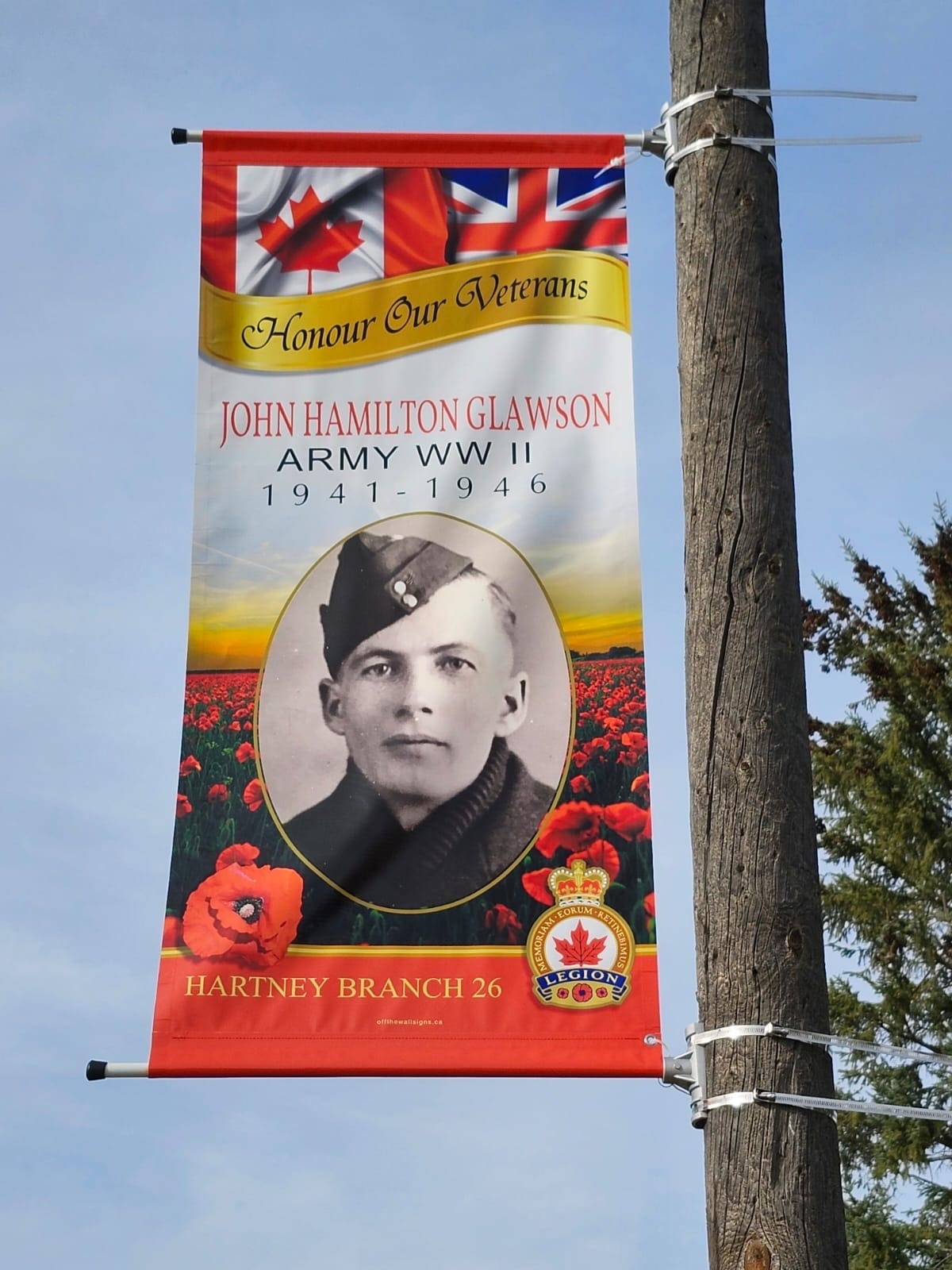 Une bannière colorée sur un mât avec un portrait de John Glawson et le texte Honour Our Veterans (Honorons nos anciens combattants).