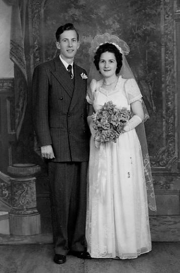 Portrait en noir et blanc d’un couple blanc souriant le jour de son mariage, la mariée tenant un bouquet.