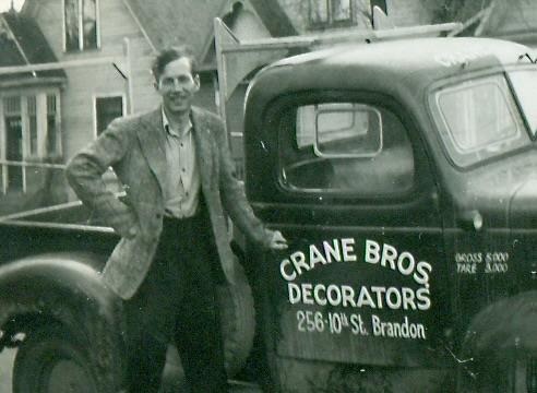 Photo en noir et blanc d’un homme blanc debout à côté d’un camion portant l’inscription Crane Bros Decorators.