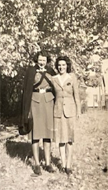 Photo sépia de deux femmes blanches vêtues d’un uniforme, debout à l’extérieur, se tenant par le bras.