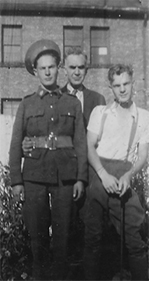 Photo en noir et blanc de trois hommes debout; l’un d’eux est en uniforme.