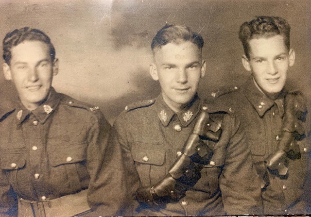 Photo sépia de trois hommes blancs souriants en uniforme, cadrée à partir du torse.