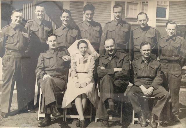 Photo sépia d’un groupe d’hommes en uniforme souriants et d’une femme en tenue d’infirmière.