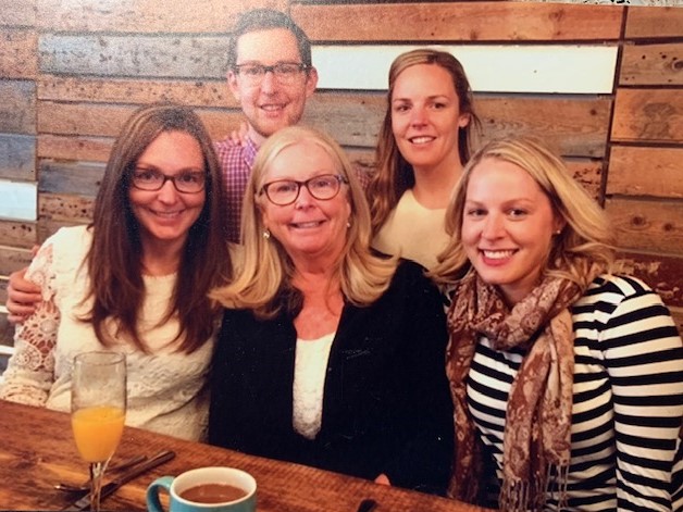 Quatre femmes blanches souriantes et un homme dans un restaurant aux murs en bois avec des boissons sur la table.